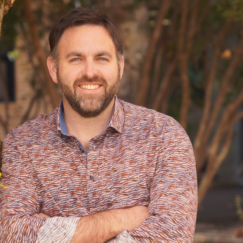 Climate Services expert Dr Tomas Remenyi smiles at the camera with his arms crossed. He wears a patterned shirt and has dark hair and a beard. 