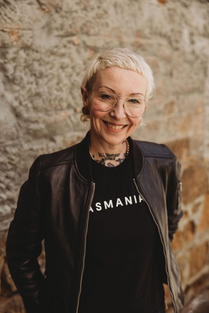 A photo of Dr Polly McGee. They smile at the camera in a black leather jacket and short cropped blonde hair.